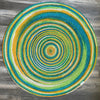 Colorful round hand-braided jute area rug with concentric circles in blue, green, yellow, orange, and white. Eco-friendly, reversible.