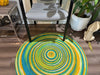 Colorful round Jute Rug featuring a concentric design. Reversible, eco-friendly area rug placed under chair.