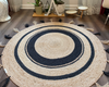 Round, hand-braided natural jute area rug featuring a black circular design, perfect for boho decor.