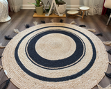 Round, hand-braided natural jute area rug featuring a black circular design, perfect for boho decor.