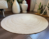 Natural, hand-braided, reversible round jute area rug in natural beige style on a dark wood floor.