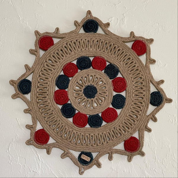Decorative wall hanging with concentric circles in beige, red, and blue on a white wall.