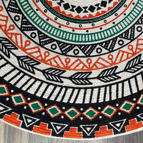 Partial view of a reversible round jute rug with a boho tribal pattern in black, orange, green, cream, and beige.