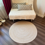 Hand-braided round jute area rug in natural beige on dark wood floor. Reversible, eco-friendly home decor.